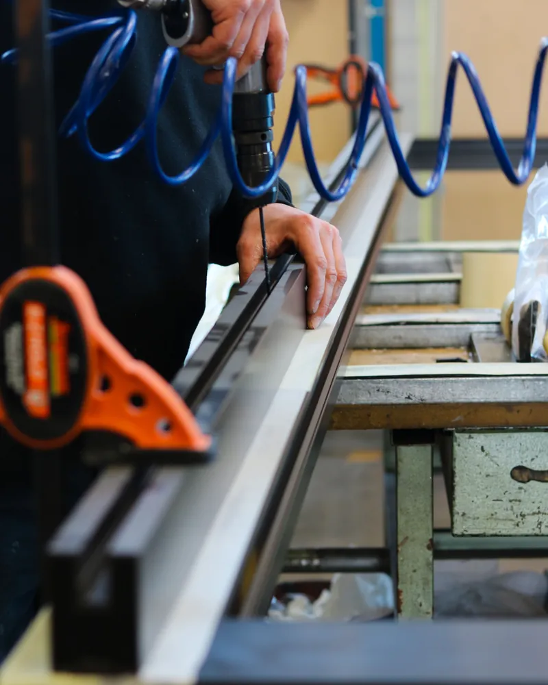 Mains mesurant un profilé métallique au mètre sur un établi