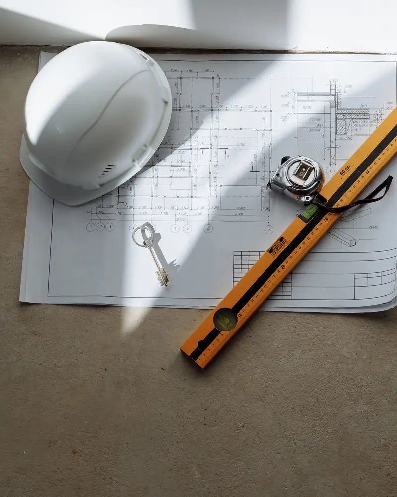 Plan de bâtiment coté, casque, mètre ruban et niveau posés sur le plan, chiffrage d'une commande de gros œuvre