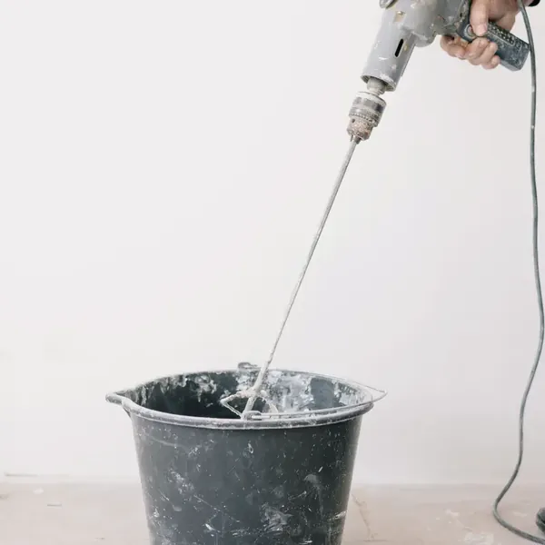 Fouet mélangeur monté sur une perceuse, au-dessus d'un seau de chantier