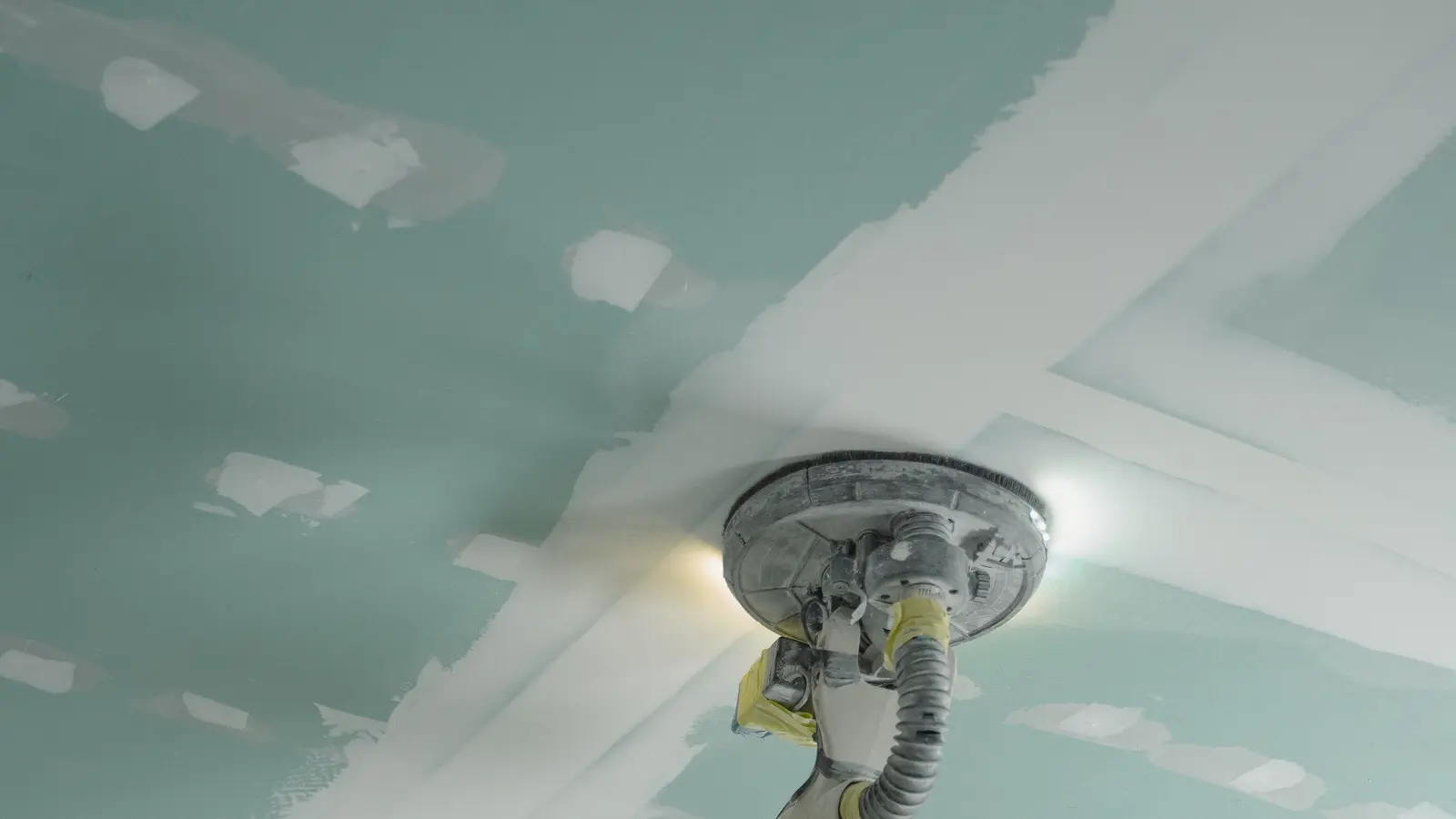 Plafond en plaques de plâtre à parement vert, joints bandés et enduits, ponceuse à plafond en action