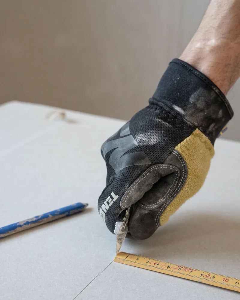 Découpe d'une plaque de plâtre au cutter le long d'un mètre pliant
